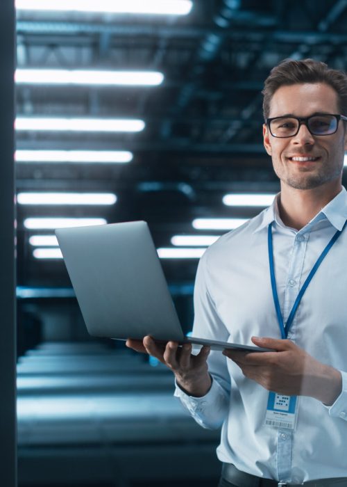 Late at Night in Private Office Male Businessman Works on a Lapt Late at Night in Private Office Male Businessman Works on a Laptop Computer. He Look at the Camera with Smile. Data Protection Engineering Network for Cyber Security. Business Concept